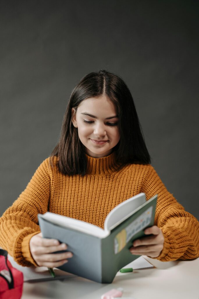 Élève assise à son bureau qui lit un livre en souriant.