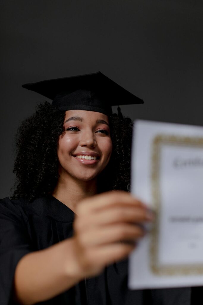 Femme portant un chapeau de gradution qui sourit en tenant son diplôme.