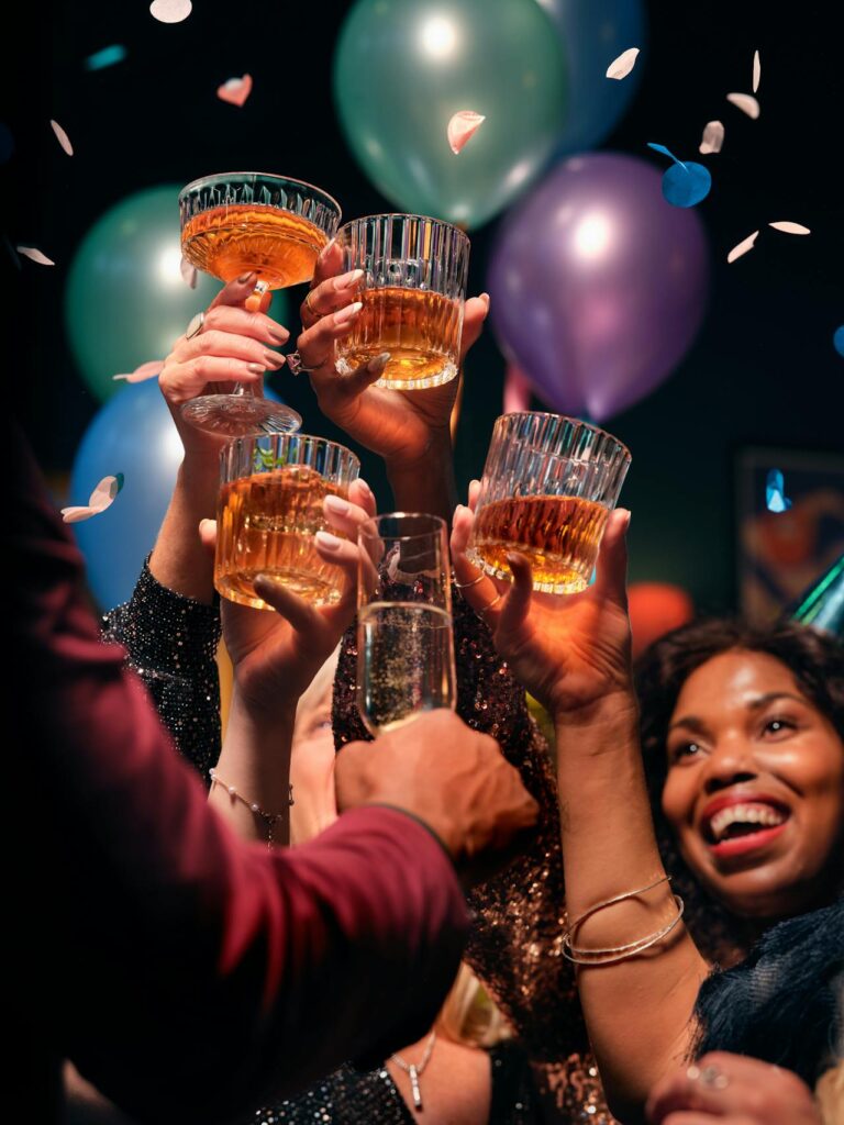 Groupe d'amis qui lève leur verre ensemble. Il y a des ballons et des confettis autour d'eux.