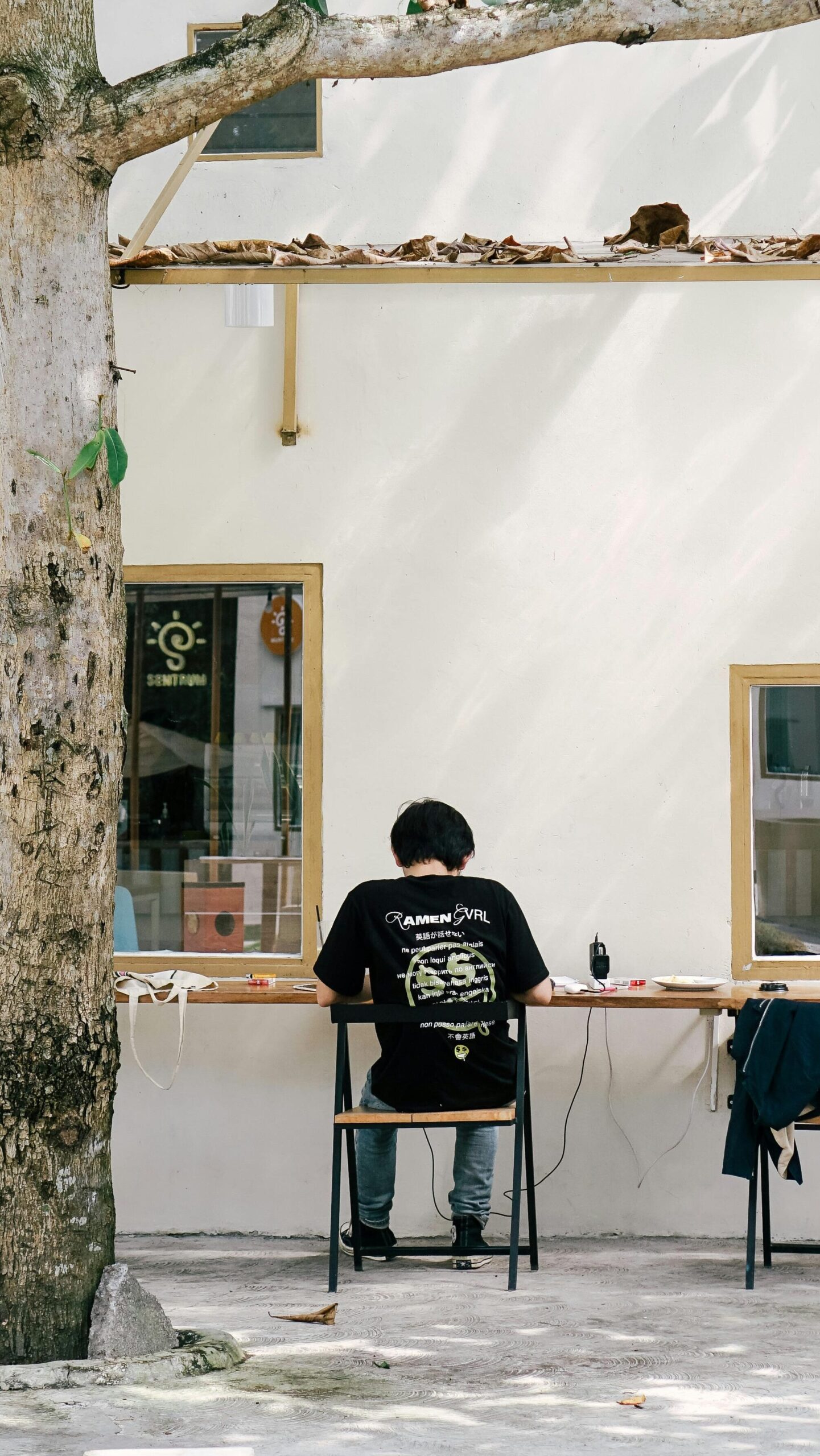 Étudiant assis à une table  extérieure d'un café pour étudier. Vue de derrière.